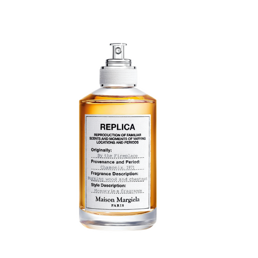 A bottle of Maison Margiela Replica perfume with amber liquid in a clear glass bottle, featuring a white label with black text and a silver spray nozzle, set against a plain white background.